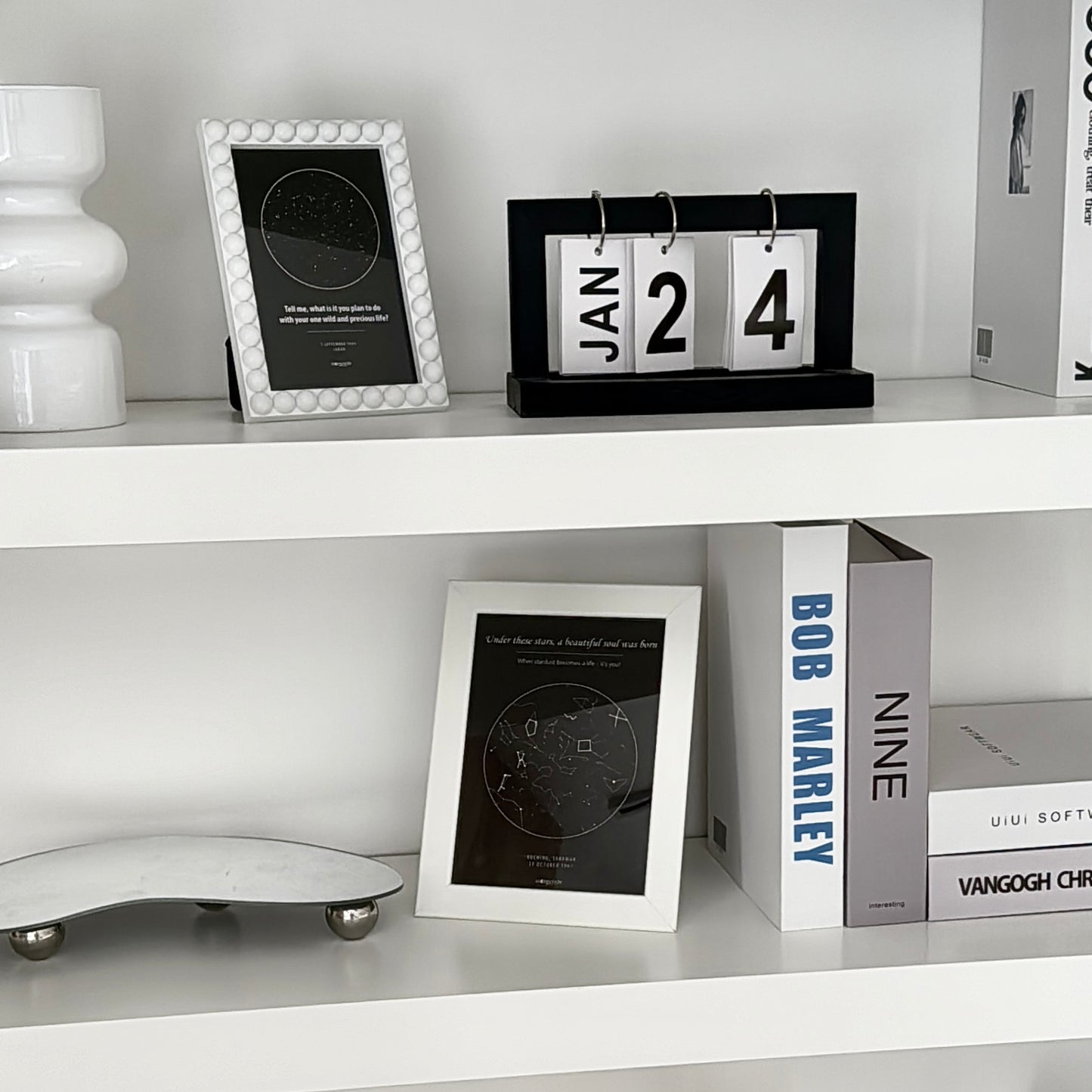 White shelf with framed star map, decorative items including a vase and a calendar.