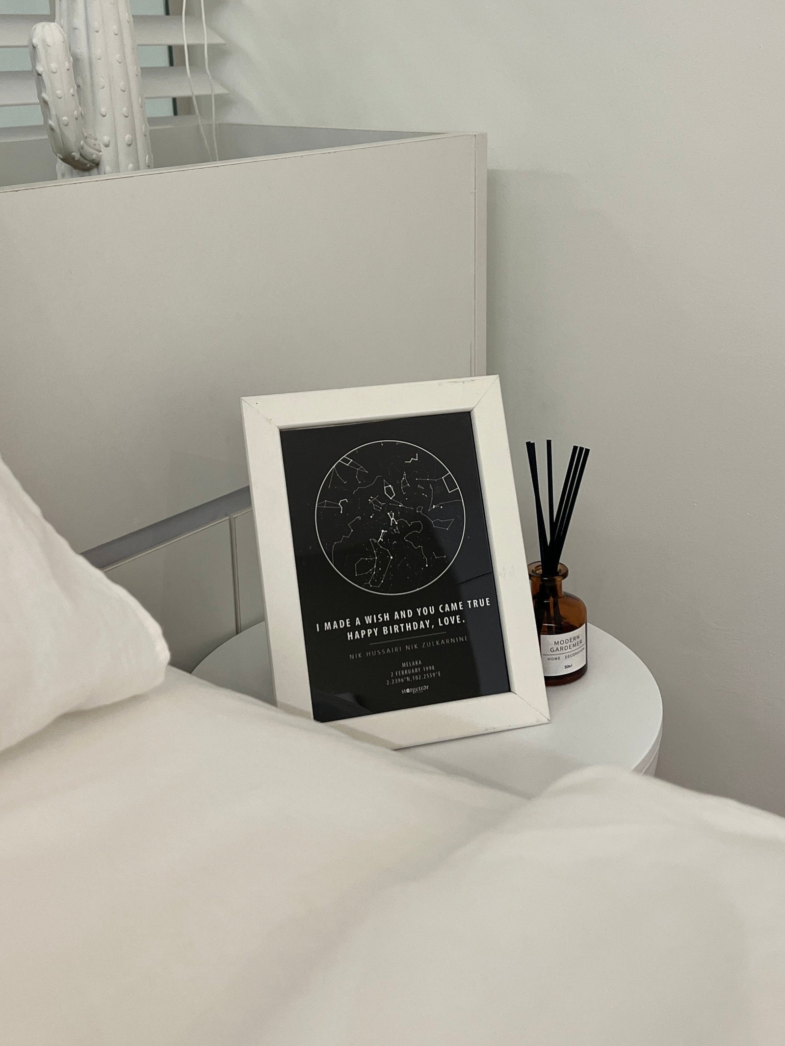 Framed custom star map print with the message ‘I made a wish and you came true. Happy Birthday, Love,’ placed on a bedside table in a minimalistic bedroom."