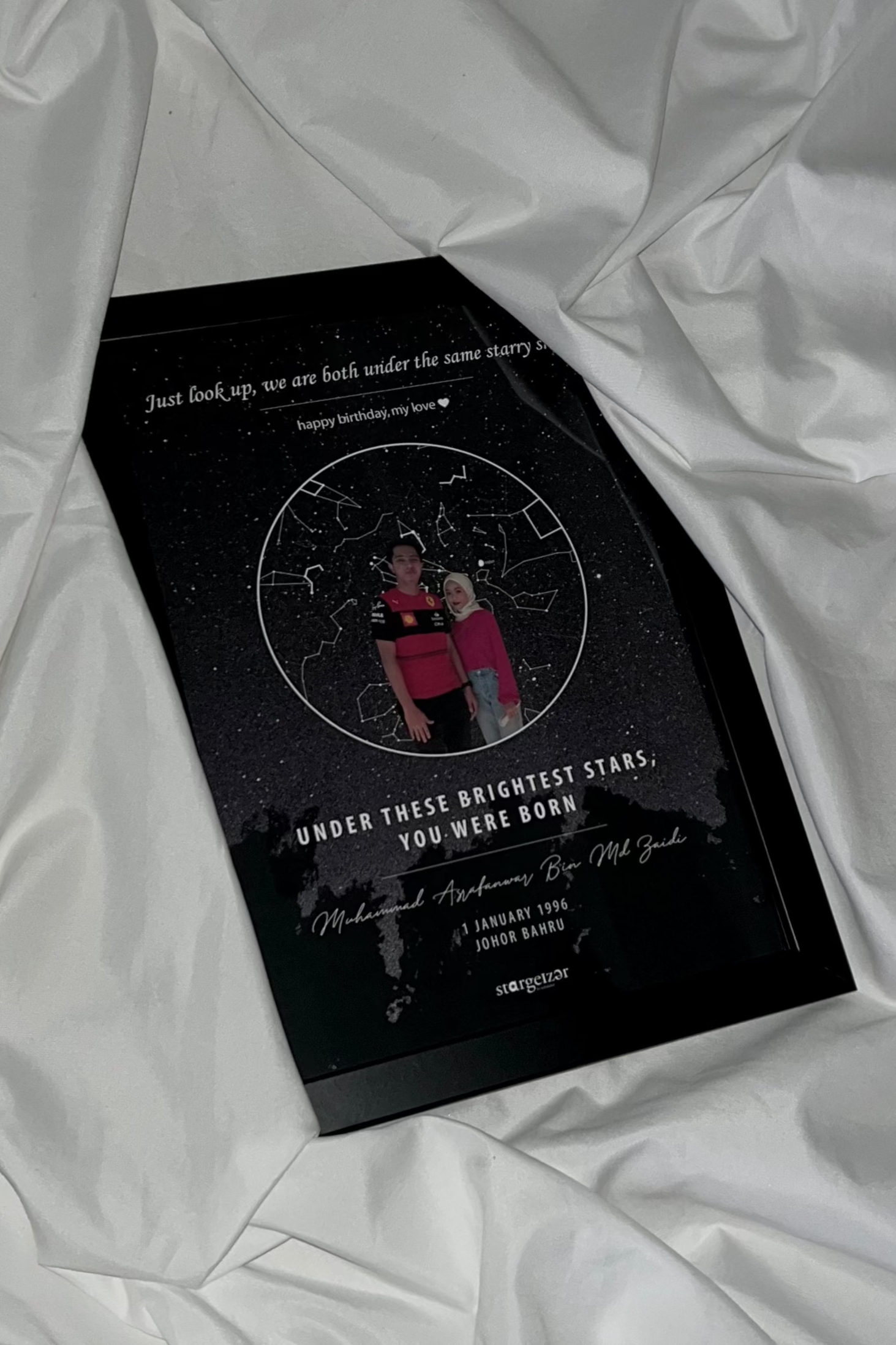 Framed custom star map with a couple’s photo inside circular constellation design, birthday dedication text, styled on satin fabric.