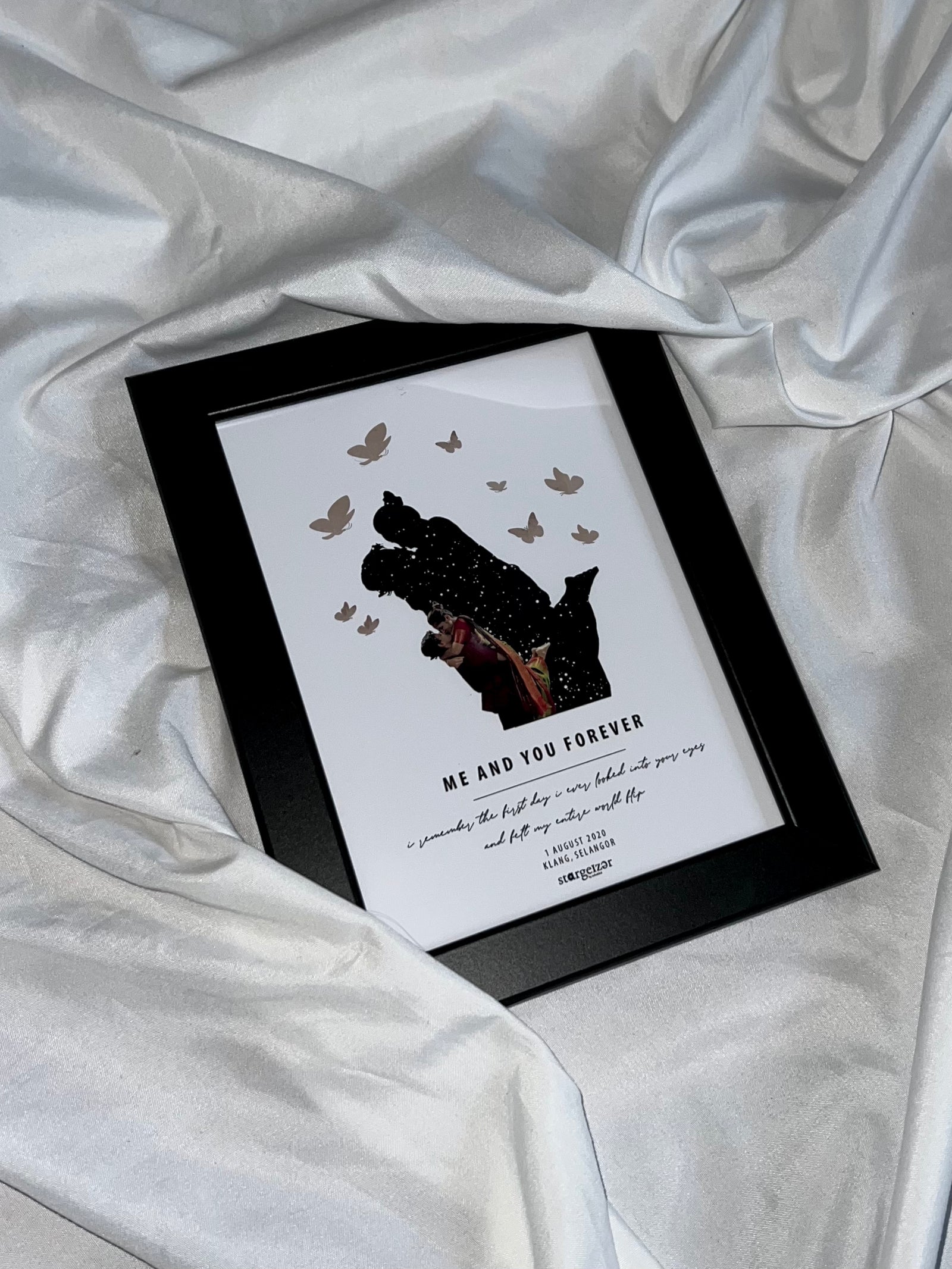 Framed custom star map with silhouette of a couple surrounded by butterflies, romantic dedication text, displayed on satin fabric.