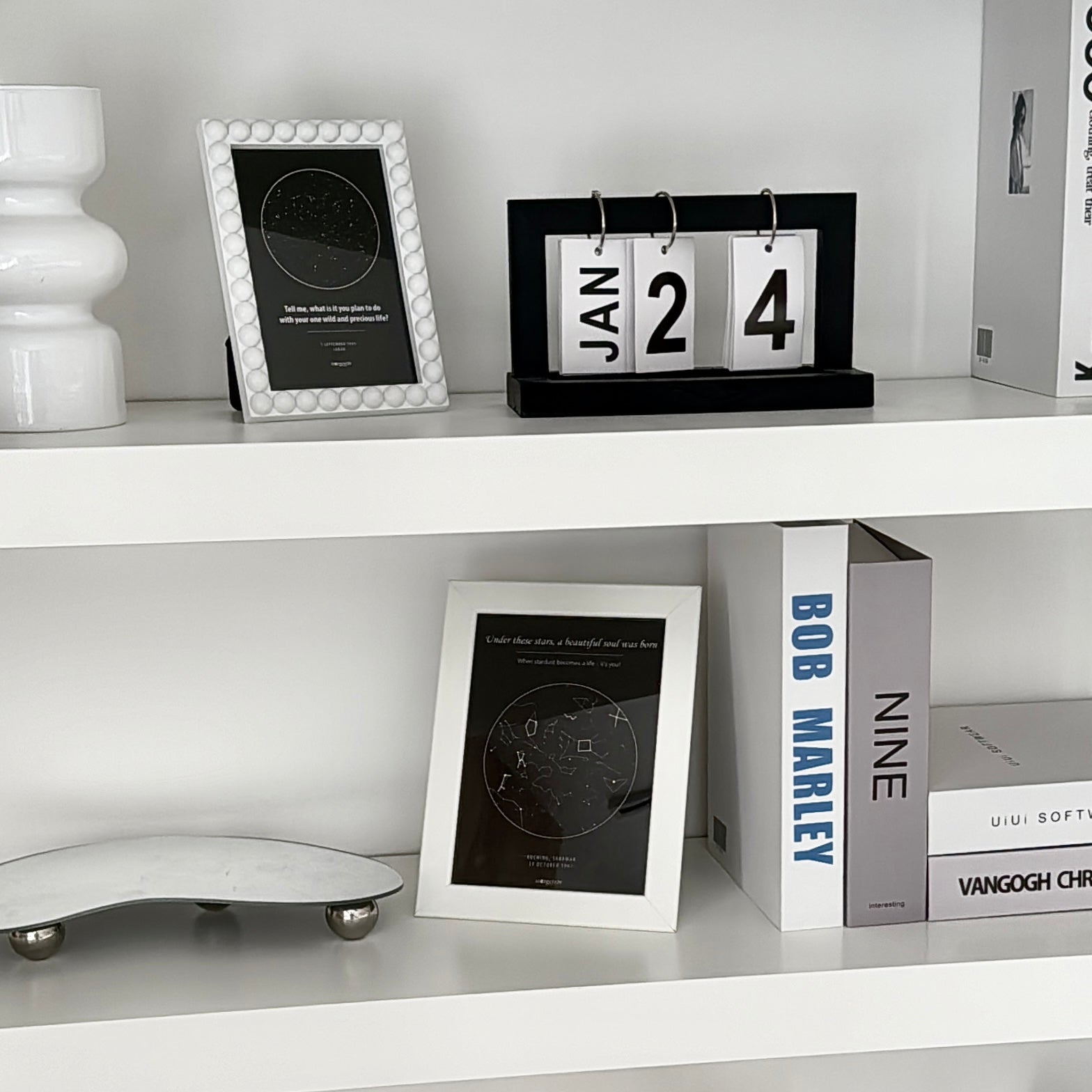 White shelf with framed star map, decorative items including a vase and a calendar.
