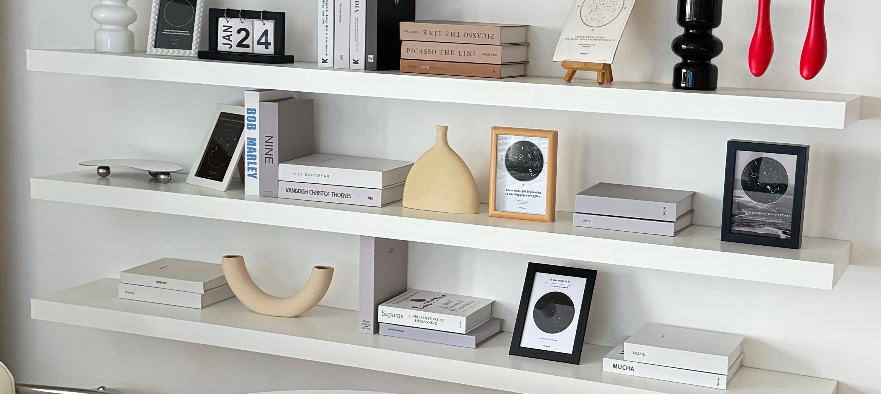 Modern white shelves decorated with books, vases, and framed custom star maps on display.
