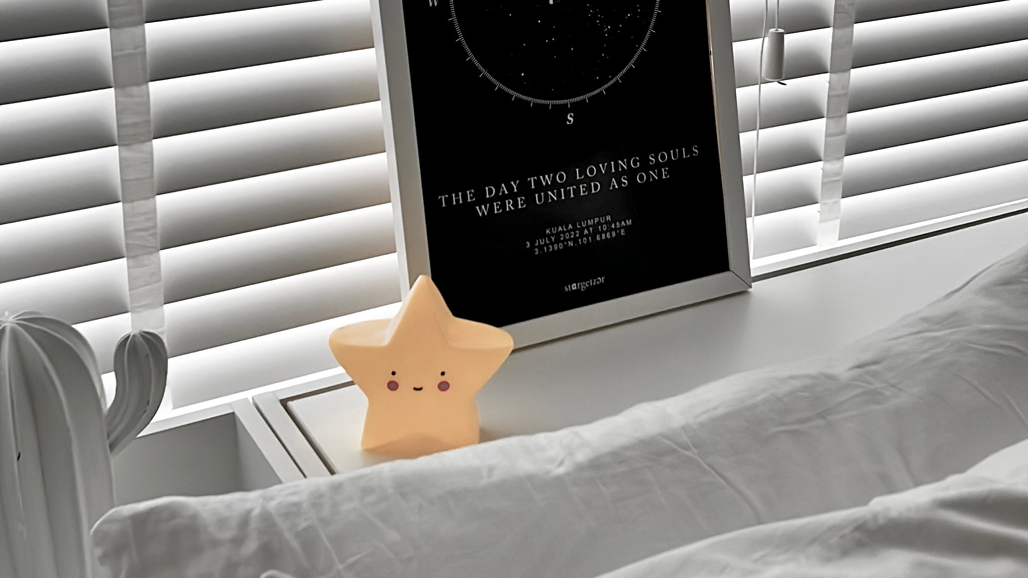 Framed custom star map print with the quote 'The day two loving souls were united as one,' displayed on a bedside table with a small star-shaped night light.