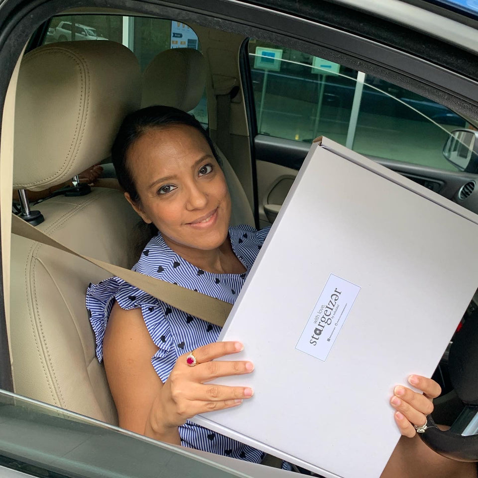 Woman smiling in her car holding a Stargeizer star map gift box, ready to be given as a present.