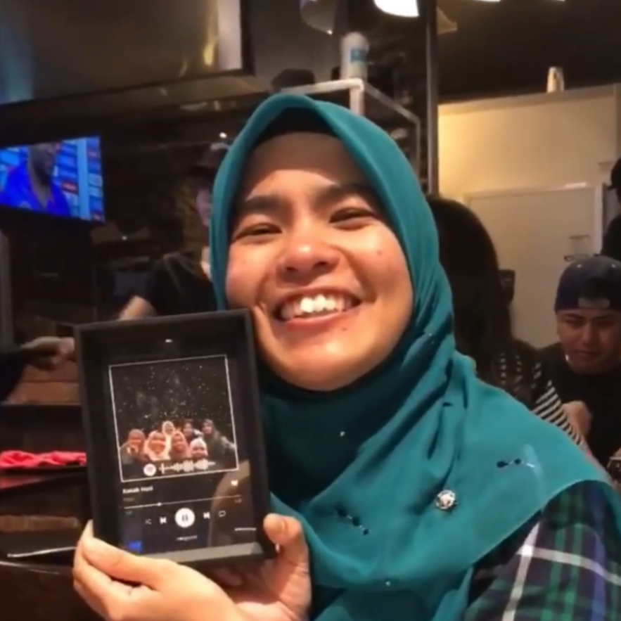 Smiling woman in hijab holding a personalized framed Stargeizer star map indoors.