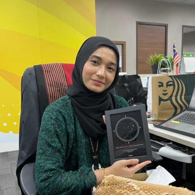 Woman sitting at an office desk holding a personalized Stargeizer star map.
