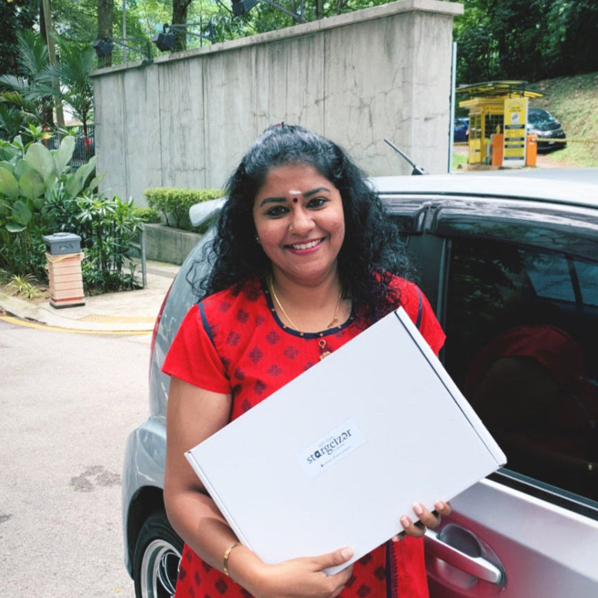 Smiling woman holding a Stargeizer star map gift box outside her car.