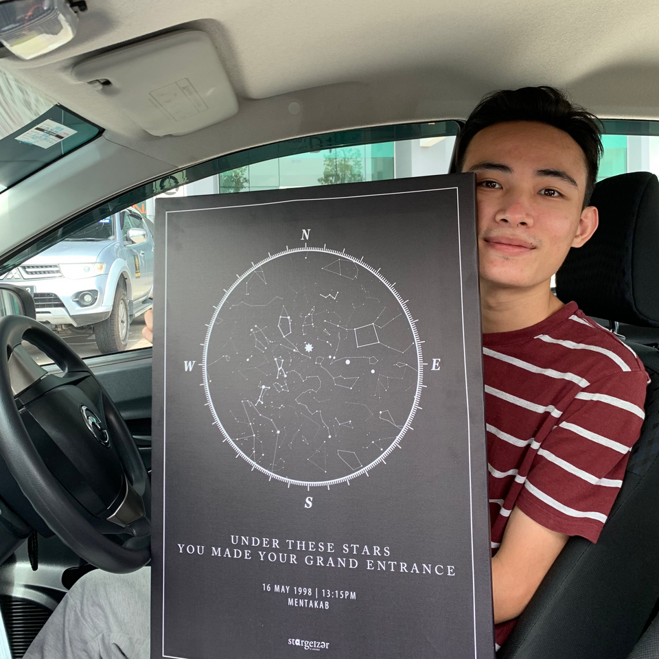 Young man sitting in a car holding his personalized Stargeizer star map poster.