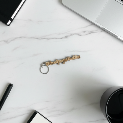 Wood Stargeizer keychain with text on a marble surface with a laptop, pen, and coffee cup.