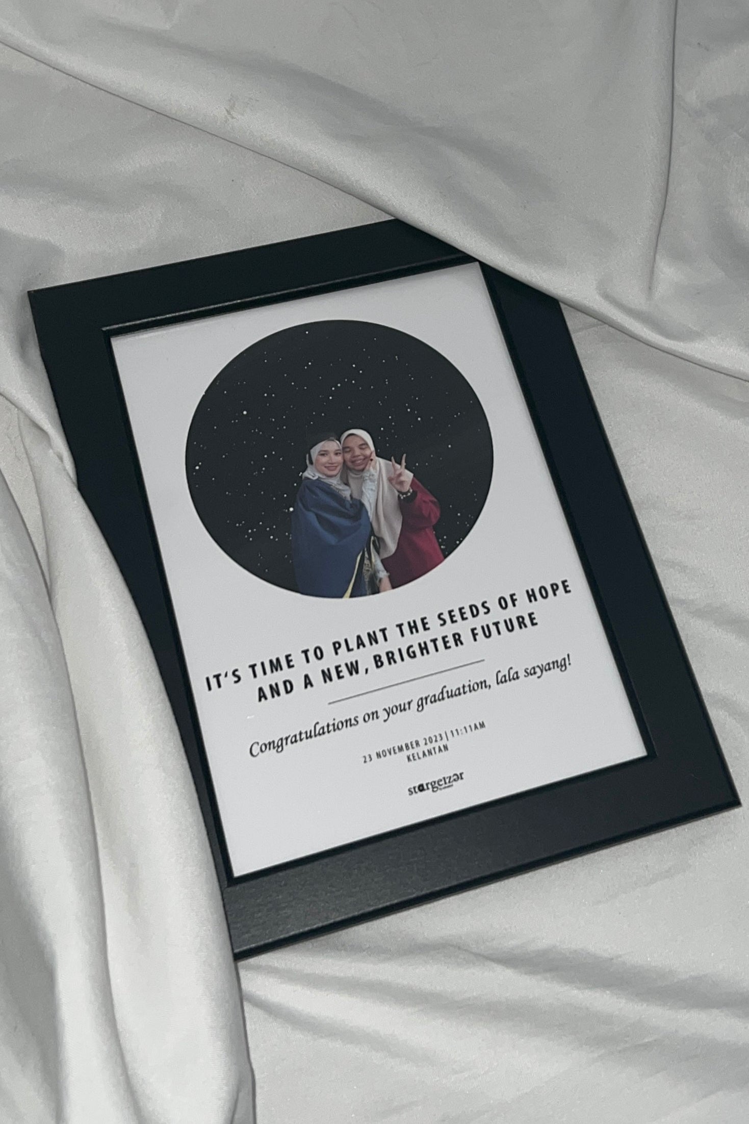 Framed star map as graduation gift with graduation photo and motivational message, styled on white satin fabric backdrop.