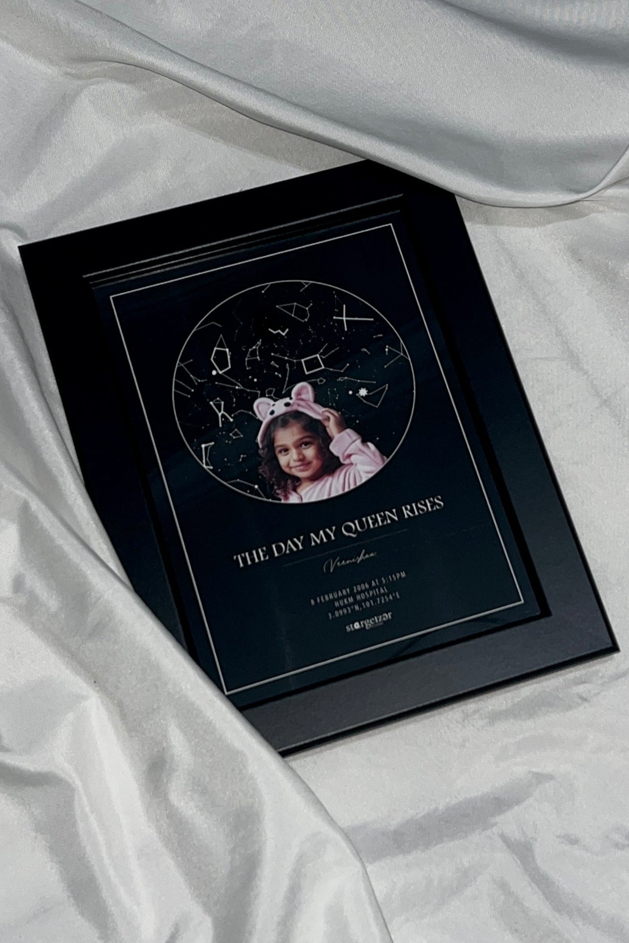 Framed star map with child’s portrait and personalized birthday message, displayed on soft satin fabric.