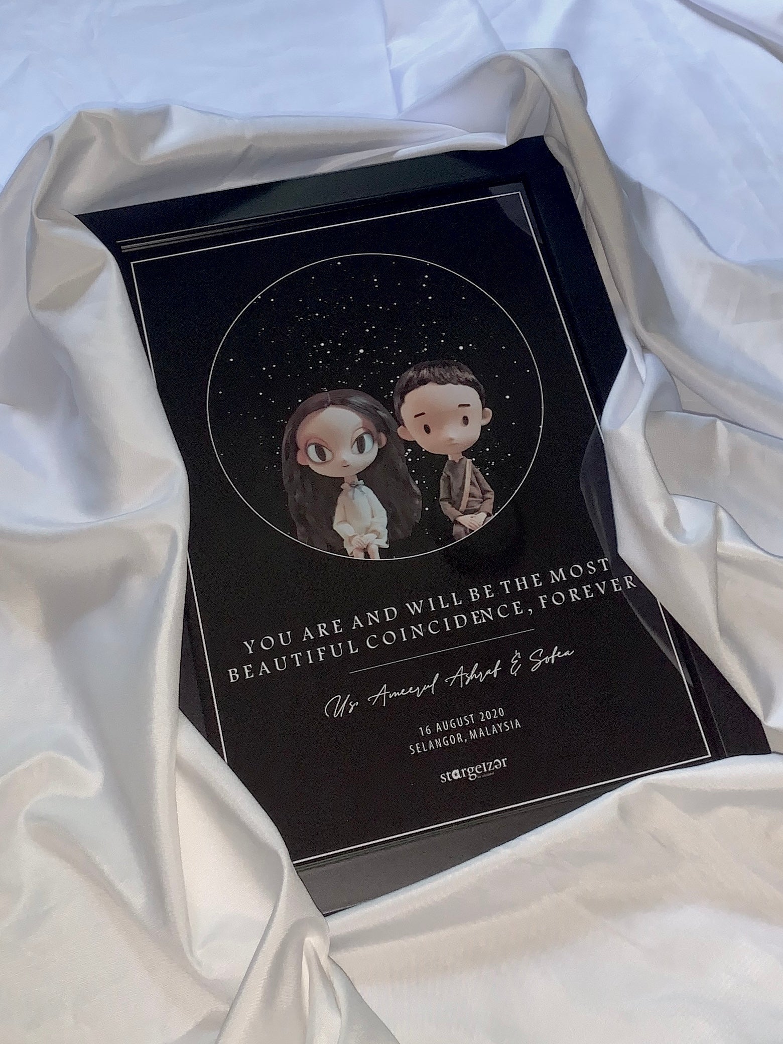 Framed custom star map with illustrated cartoon couple artwork and romantic dedication, set on draped silky fabric.