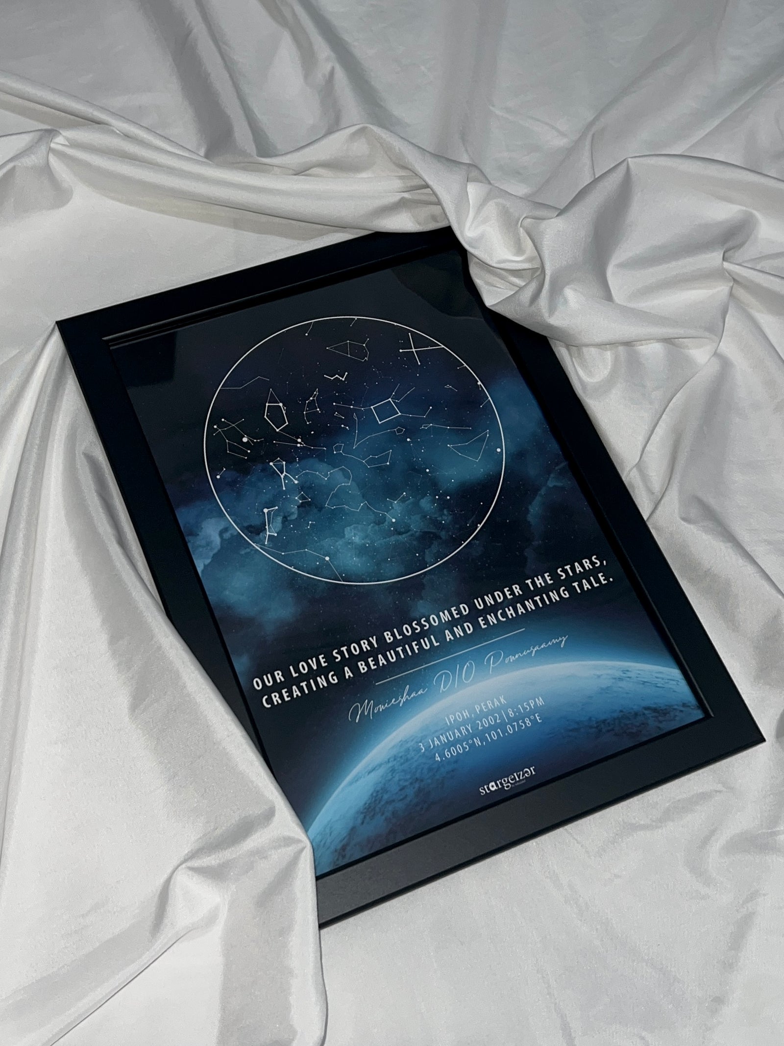 Framed star map with galaxy blue background and personalized love message, styled on satin fabric backdrop