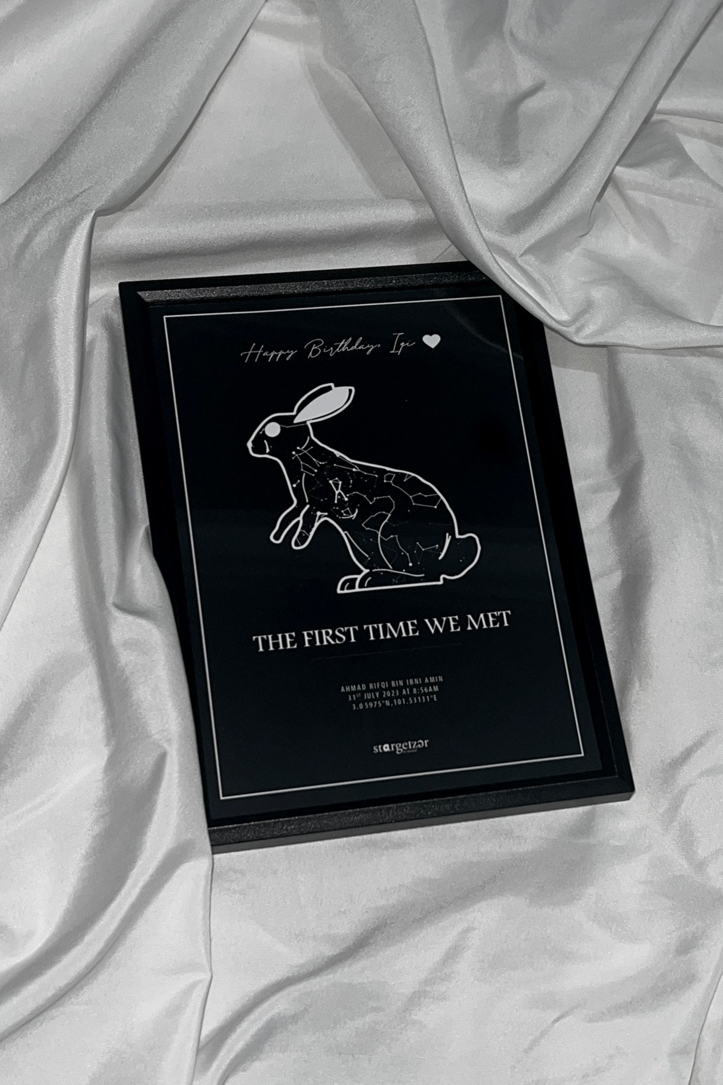 Framed star map in the shape of a cat with personalized name and date engraving on a silky white fabric background.