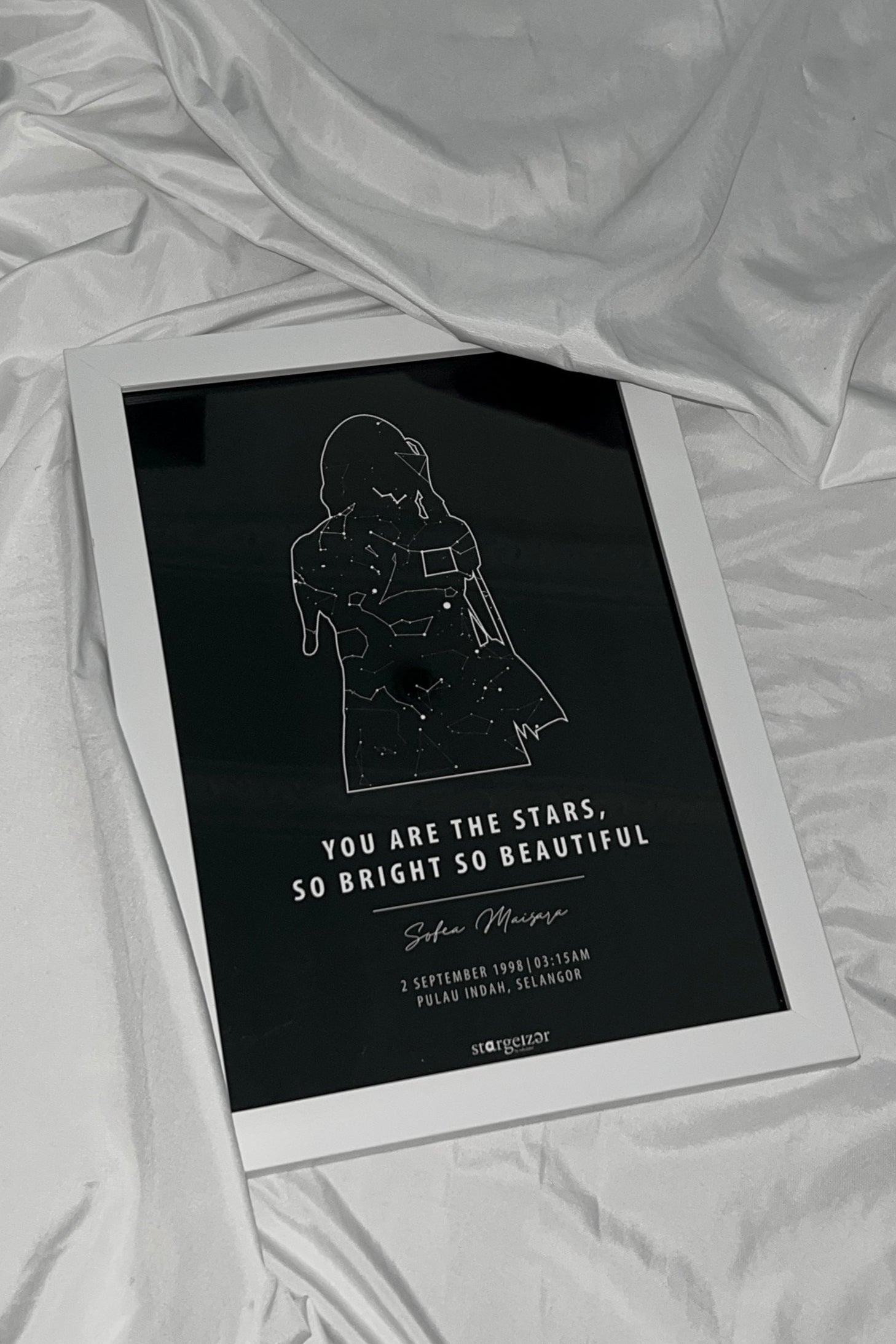 Framed star map featuring a silhouette of a girl filled with constellations and personalized quote on a white draped fabric.